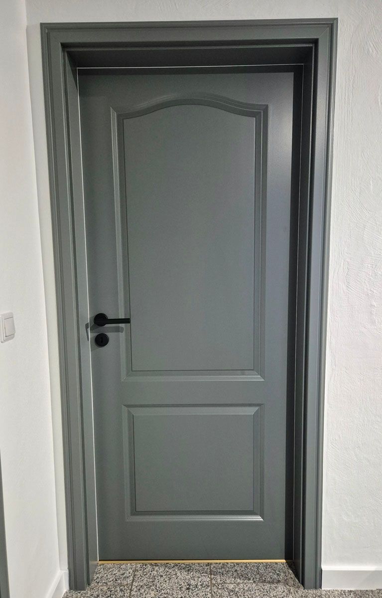 In einem Flur steht eine graue Tür mit einem schwarzen Griff.