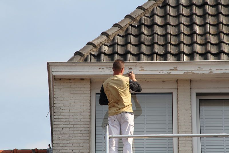 Ein Mann steht auf einem Balkon und bemalt die Seite eines Gebäudes