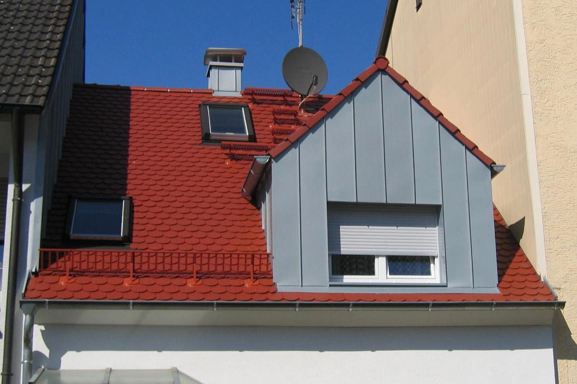 Steildach mit roter Ziegeldeckung und modern verkleideter Dachgaube.