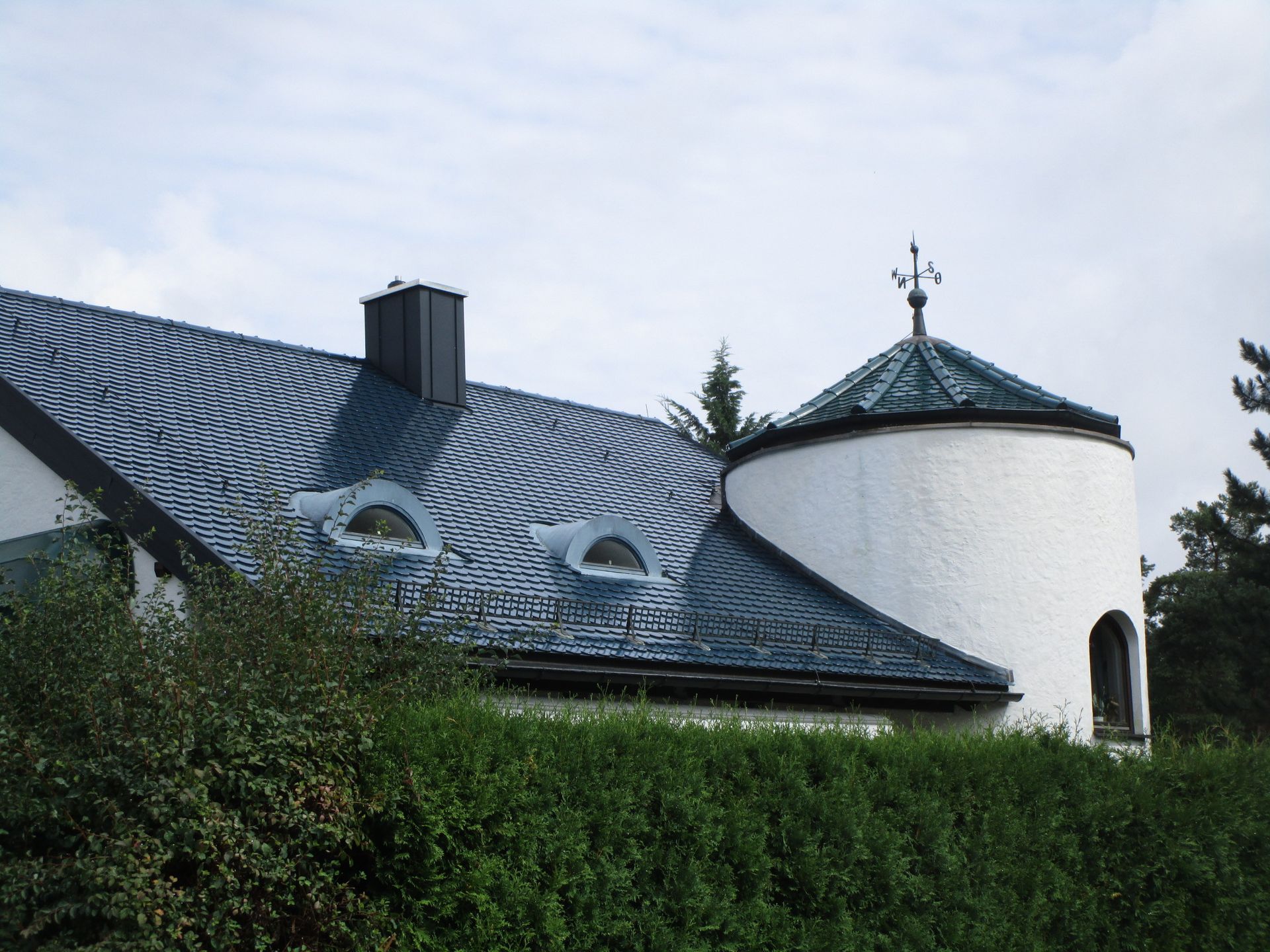 Komplexes Schieferdach mit Rundturm und Dachflächenfenstern.
