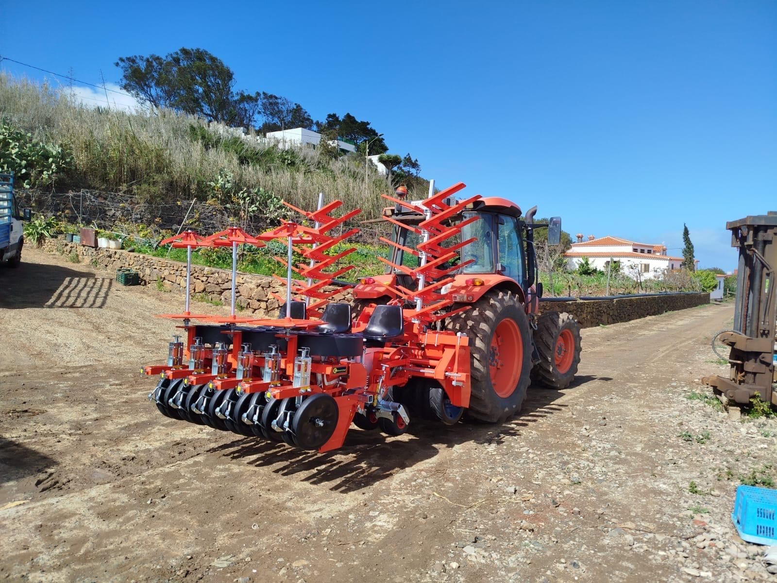 Un joven conduce un tractor rojo a través de un campo arado bajo un cielo azul despejado.
