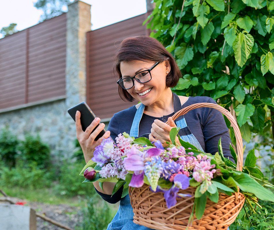 Femme portant un panier de fleurs et un téléphone portable dans la main