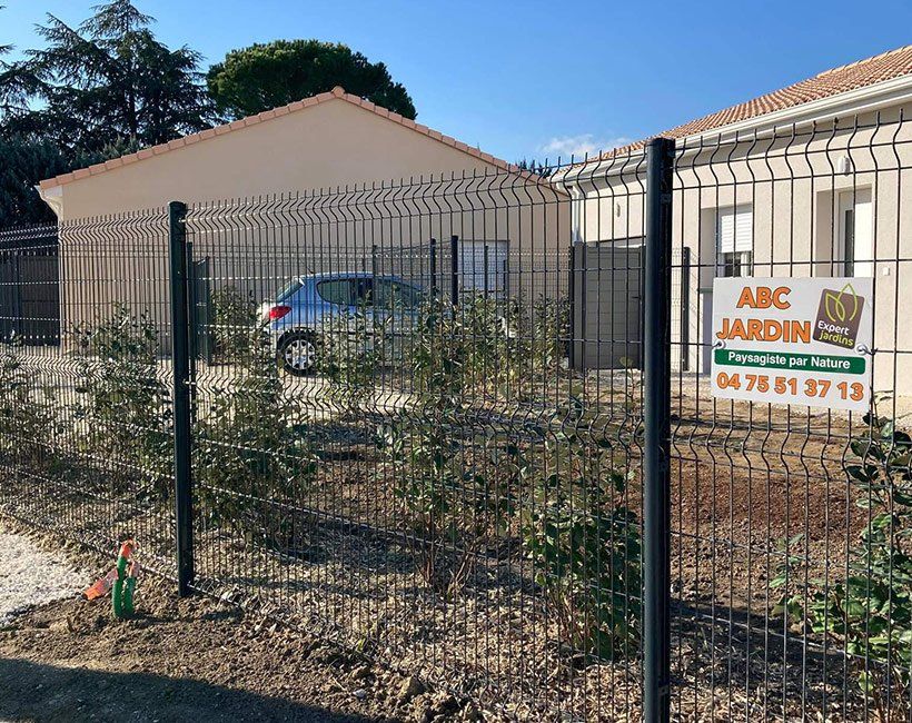 Exterieur d'une maison avec un grillage sur lequel se trouve une pancarte ABC Jardin