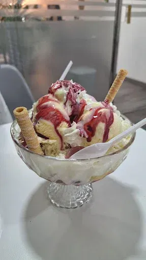 Sundae de helado en bol de cristal con barquillos y sirope de fresa.