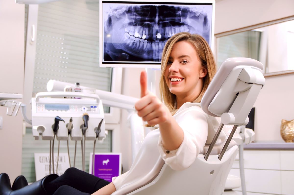 Una mujer en un sillón dental sonríe y hace un gesto de aprobación con el pulgar hacia arriba