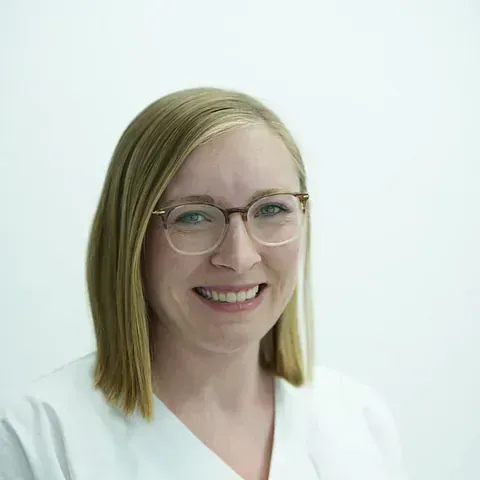 Eine Frau mit Brille und weißem Kasack lächelt in die Kamera.