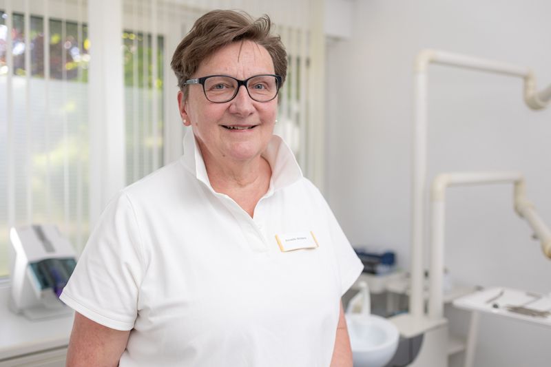 Eine Frau mit Brille und weißem Hemd lächelt in die Kamera.