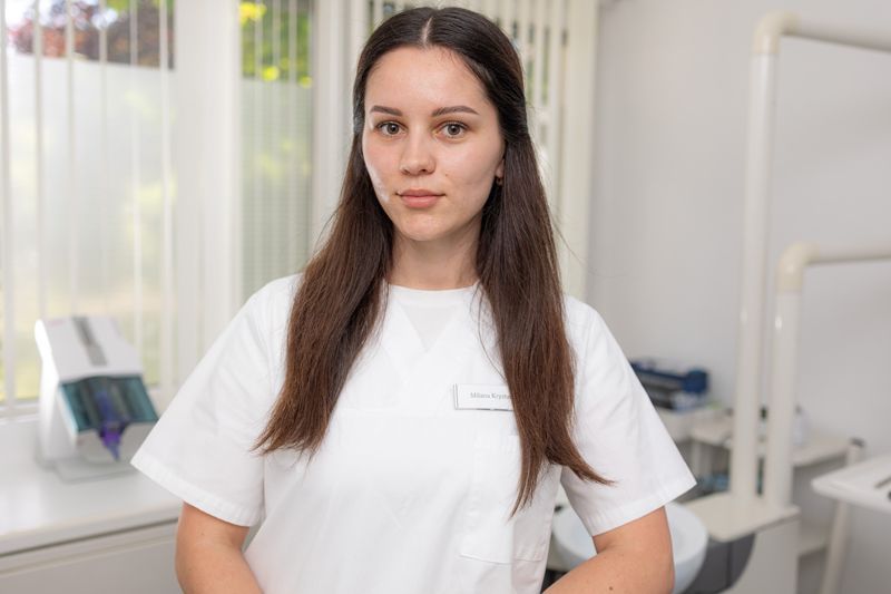 Eine Frau in einem weißen Poloshirt steht vor einer weißen Wand.