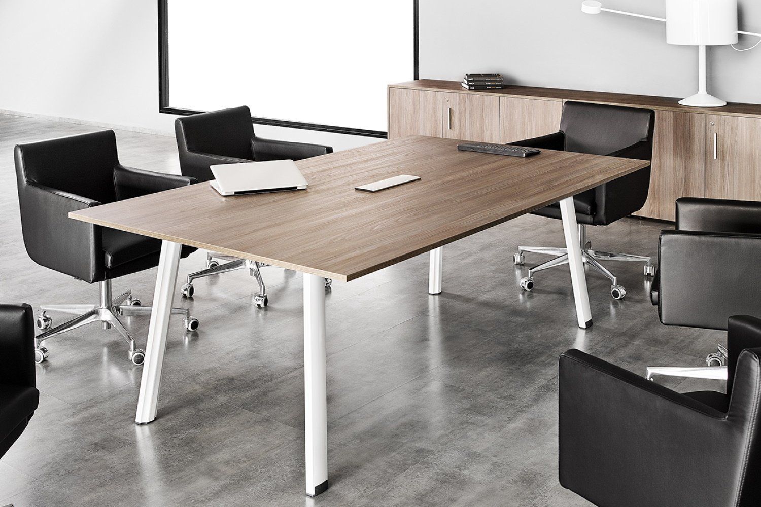 Salle de conférence avec une grande table en bois, des chaises noires et des pieds blancs.