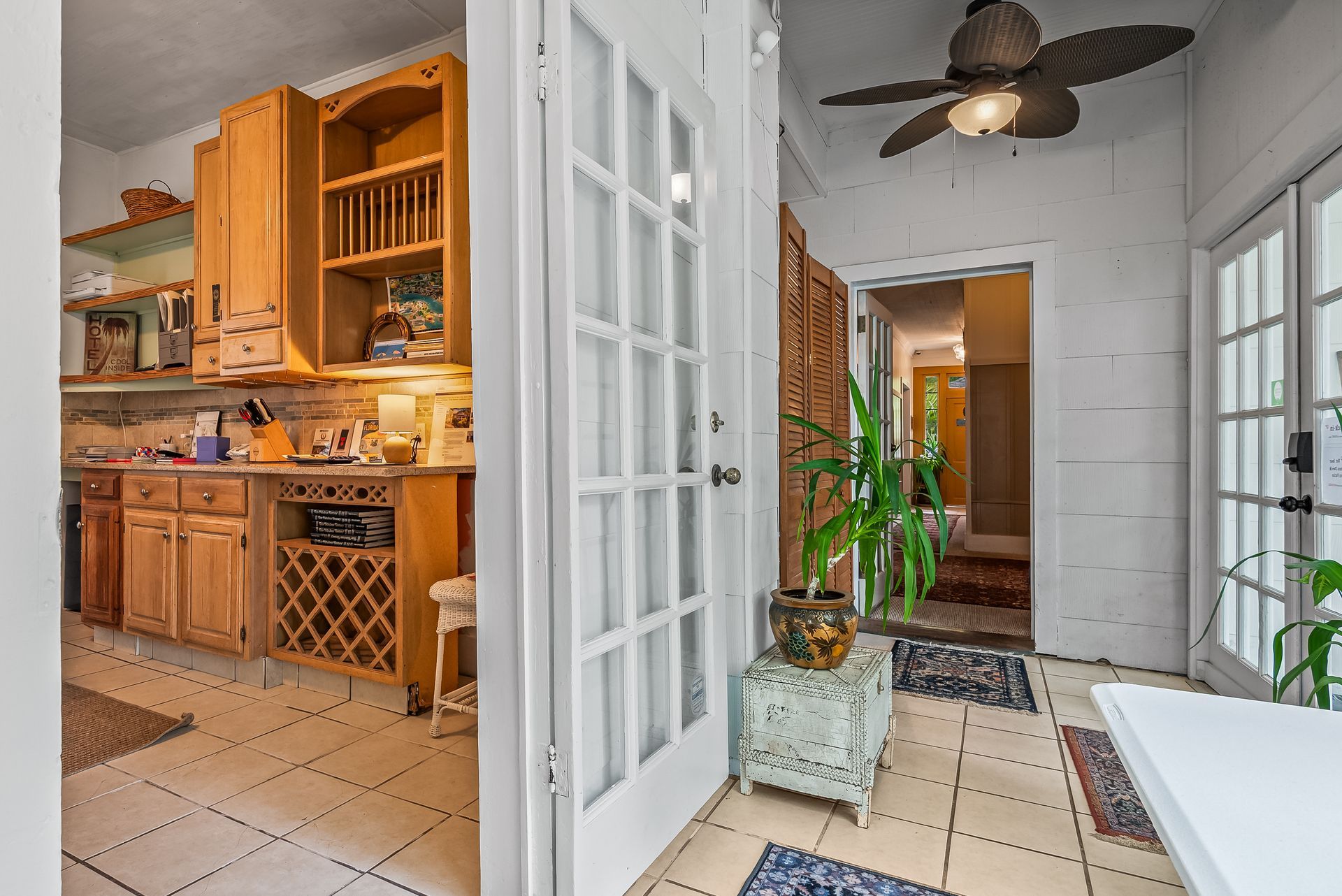 Bright kitchen hallway with French doors, wood cabinets, patterned tile, and a ceiling fan.
