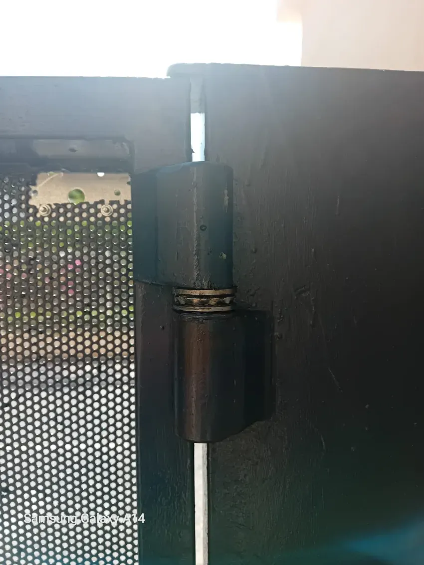 Primer plano de una bisagra de puerta de metal negro fijada a una valla y una puerta de paneles.