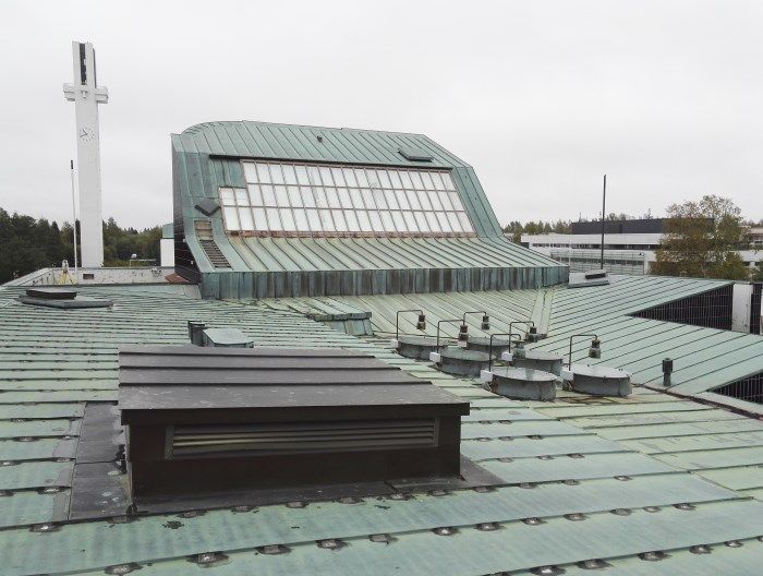 Katto vihreillä metallipaneeleilla, kattoikkunalla ja tuuletetulla rakenteella pilvisen taivaan alla