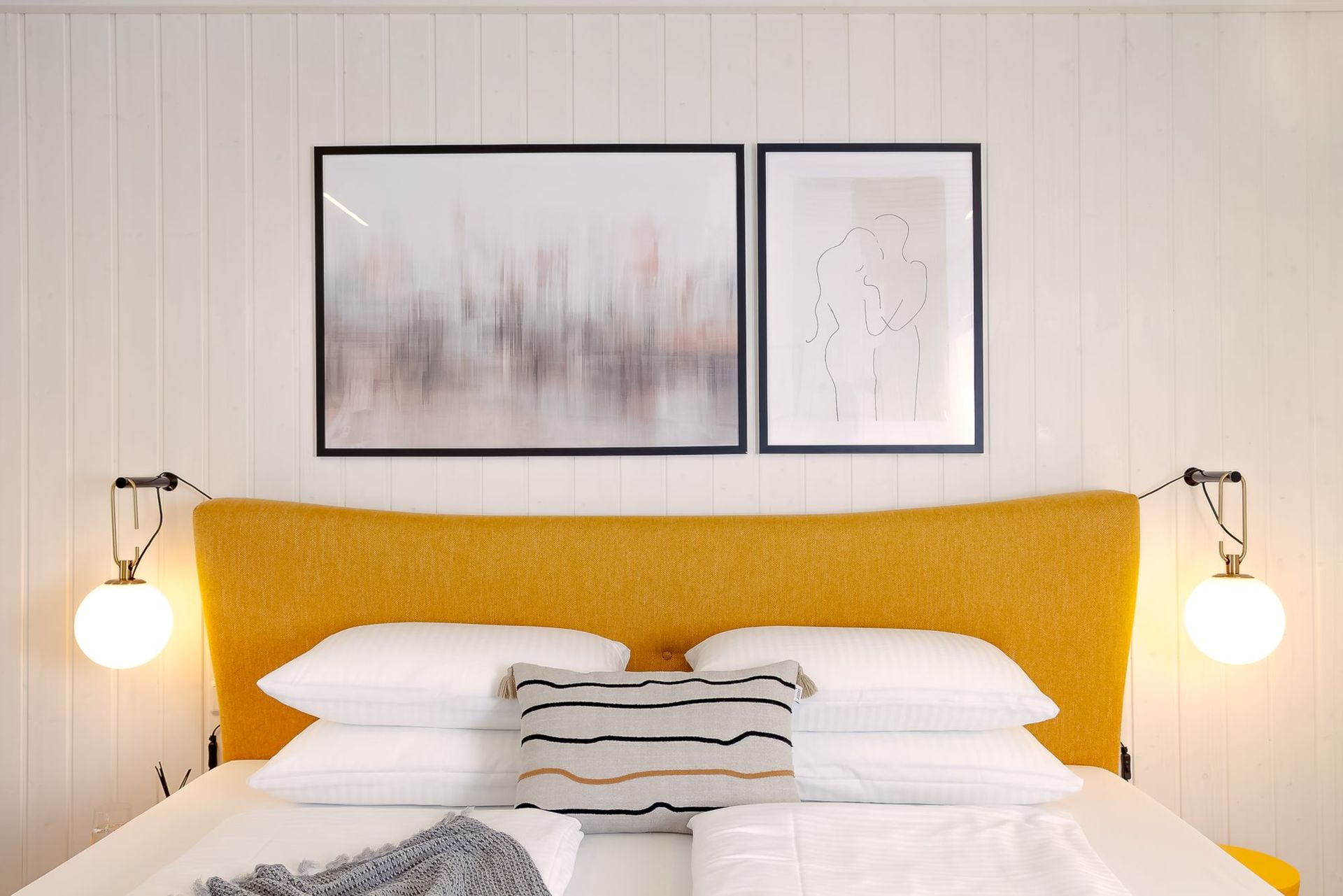 Bed with a yellow headboard, white linen and framed art