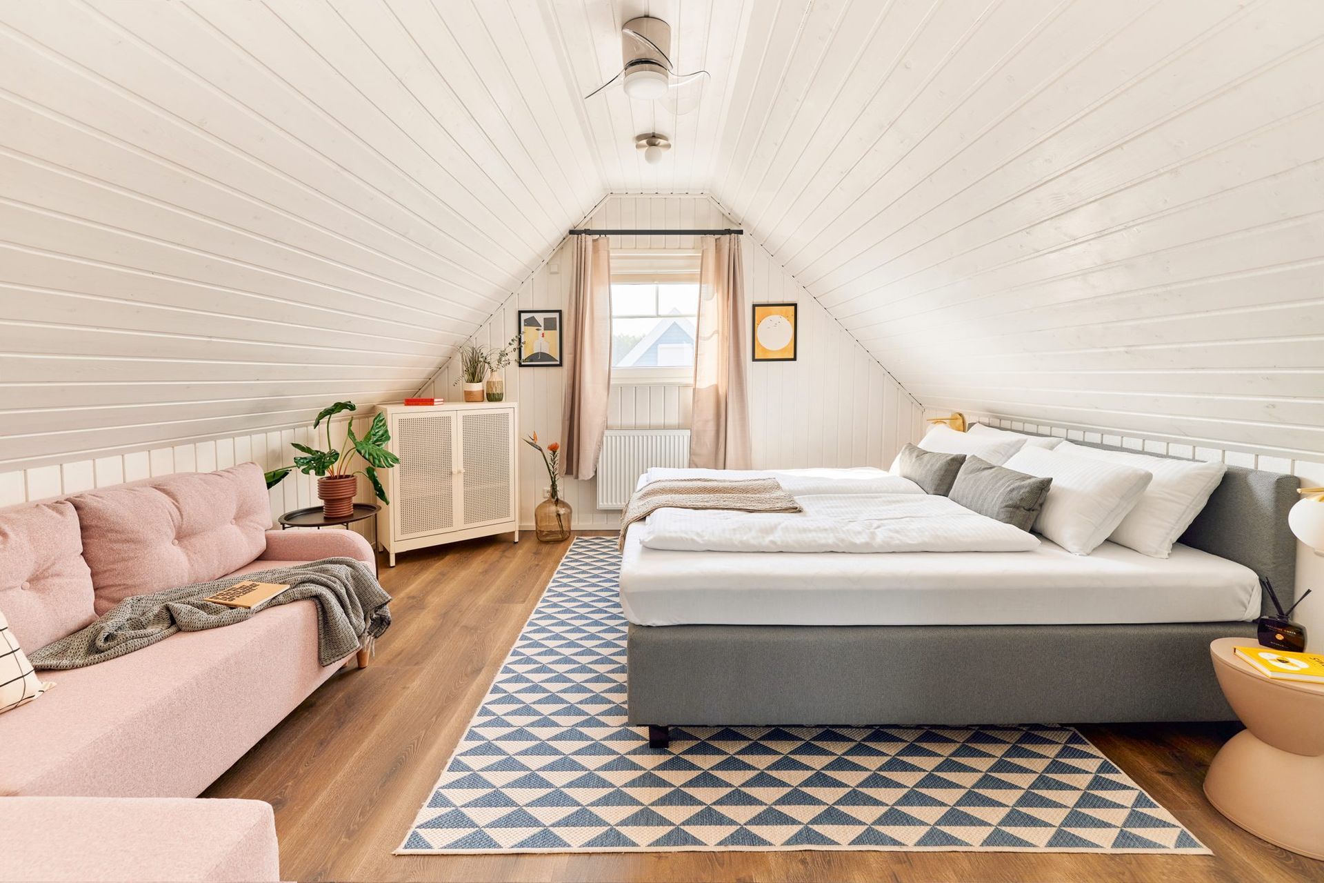 Upstairs bedroom with a queen bed and a pink sofa under the sloped ceiling