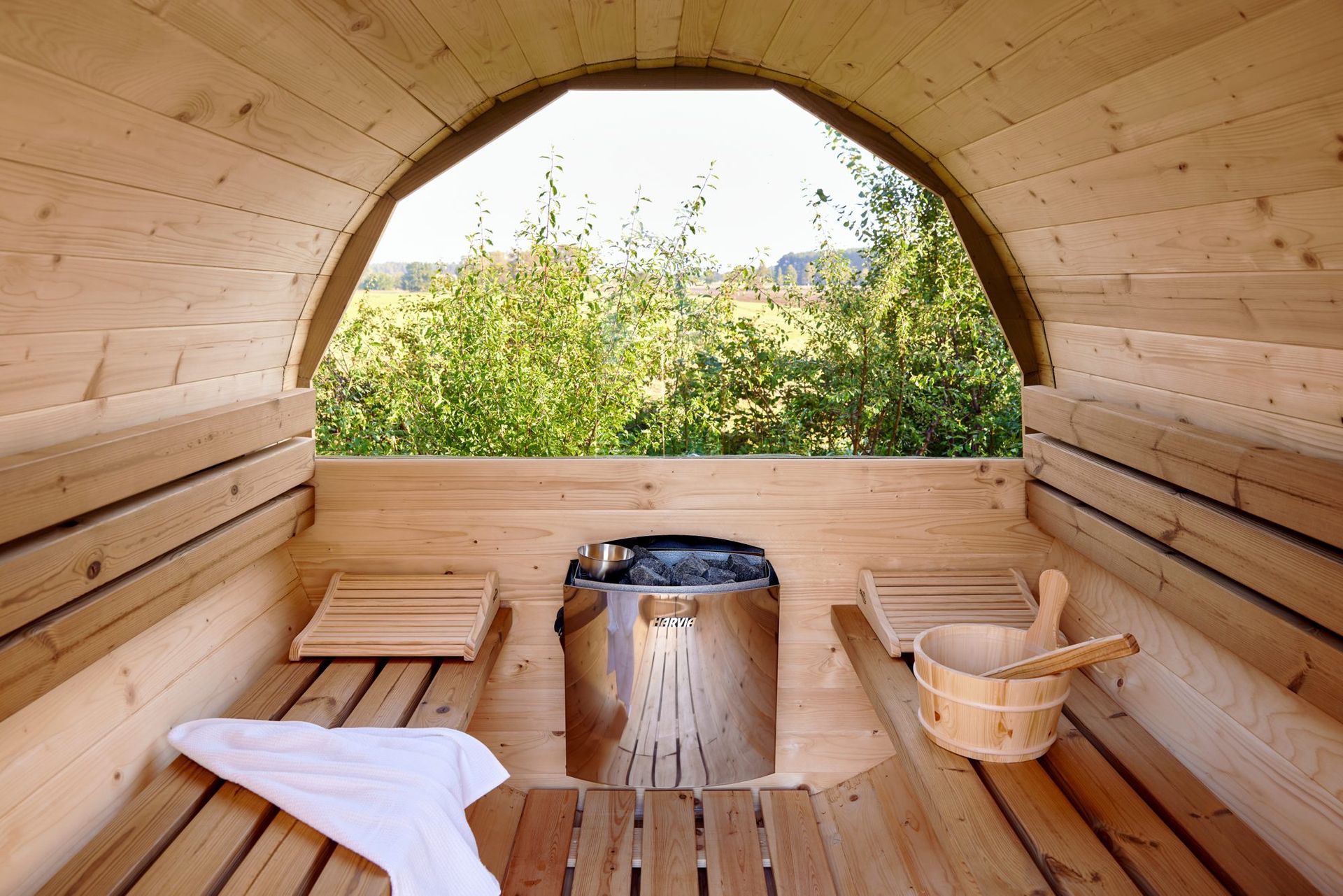 Barrel sauna interior with benches and a view of the garden