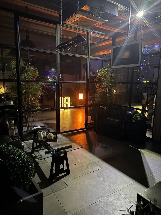 Una habitación con muchas ventanas y una mesa y sillas por la noche.