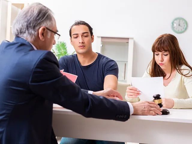 Un abogado presenta documentos a una pareja sentada a la mesa. Están discutiendo y revisando documentos.