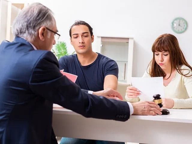 Una pareja y un abogado en una mesa; el abogado sostiene un mazo.