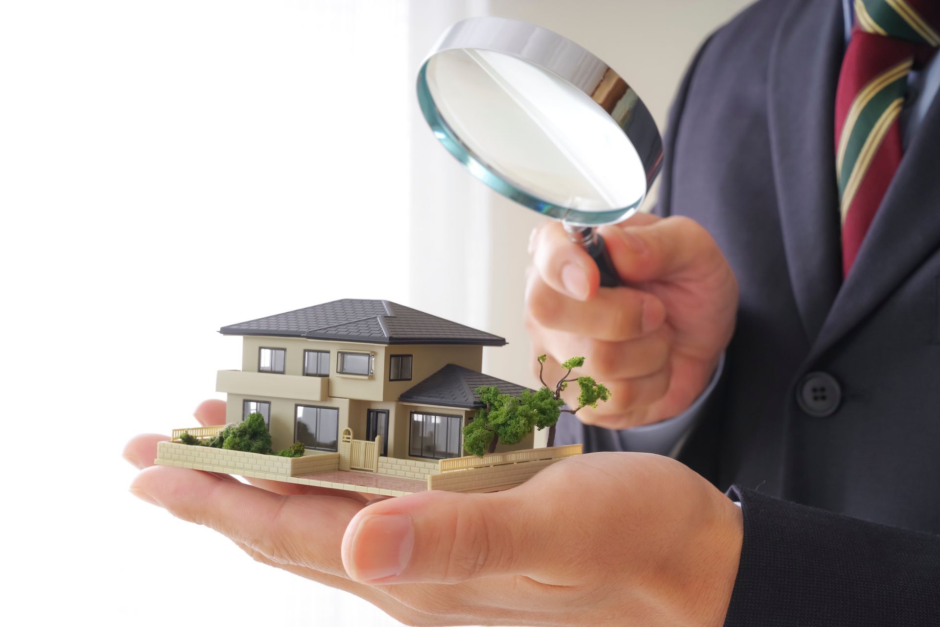 Main tenant une maison miniature examinée à la loupe