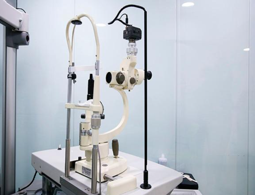 Un biomicroscopio de lámpara de hendidura blanco utilizado para exámenes oculares, colocado sobre una mesa en un entorno clínico.