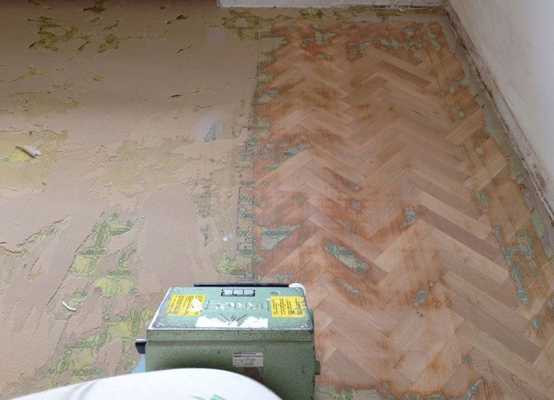 Eine Person schleift mit einer Maschine einen Holzboden.