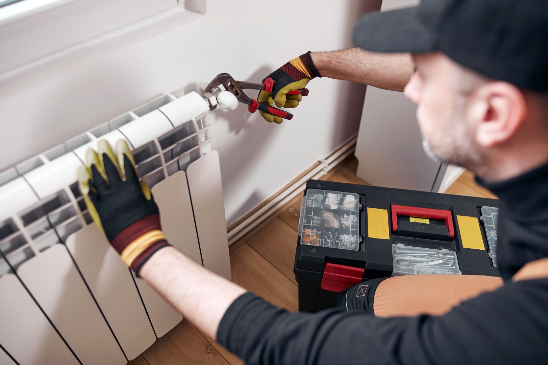 Un homme répare un radiateur avec une clé.