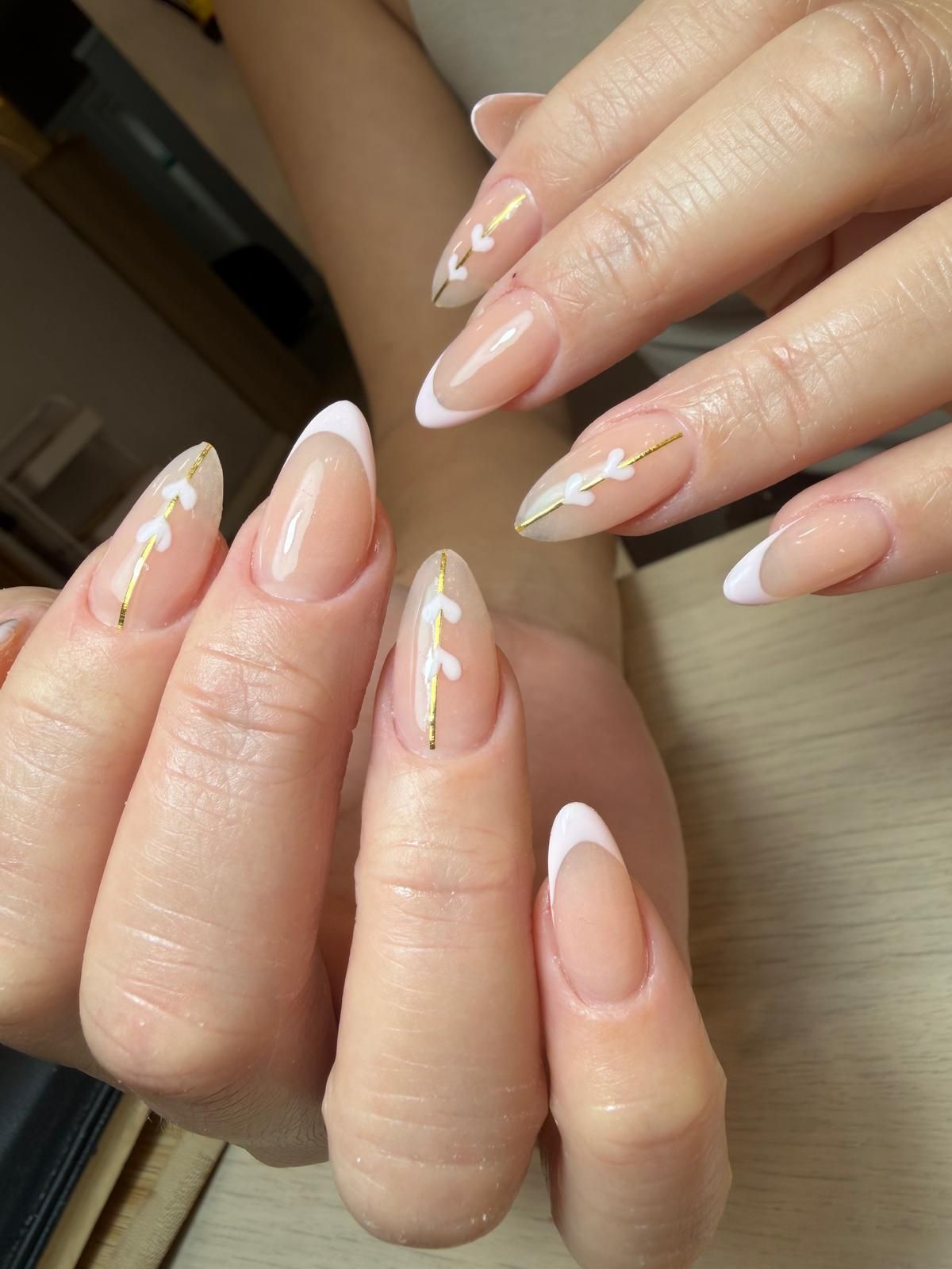 Manos con uñas brillantes de color rojo oscuro en forma de almendra se cruzan frente a un espejo de salón borroso.