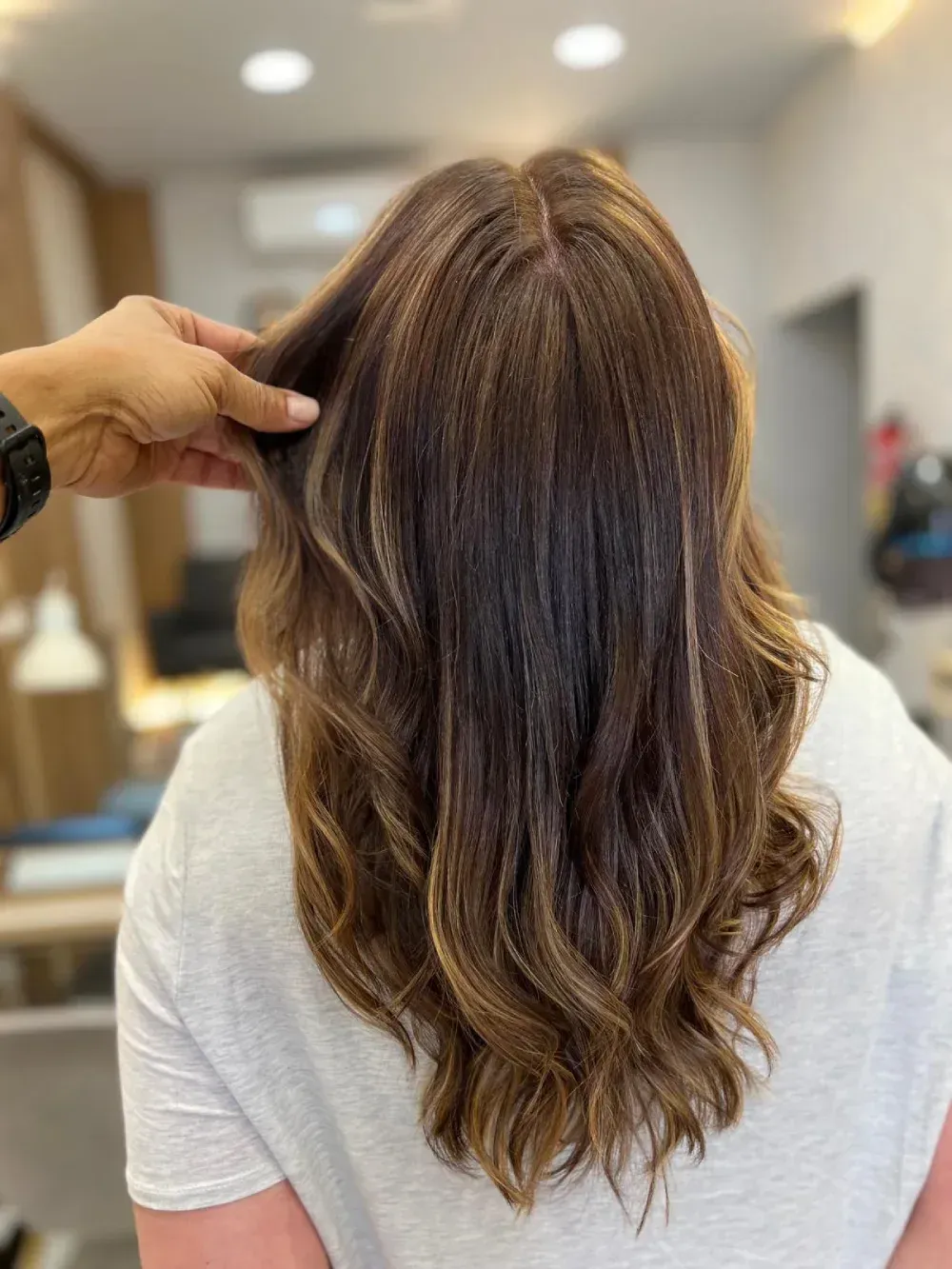Persona con cabello largo castaño de espaldas en una peluquería, mostrando las puntas en capas.