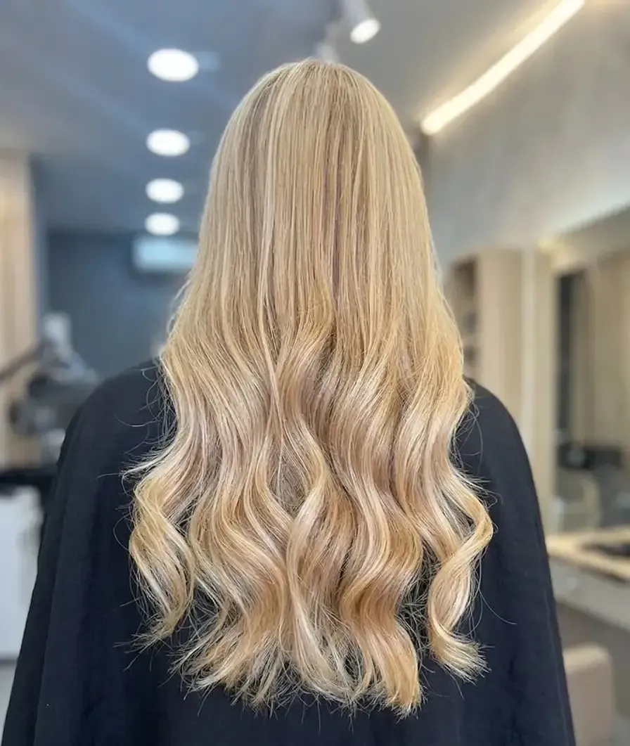Vista posterior de una larga melena rubia ondulada en un salón de belleza.