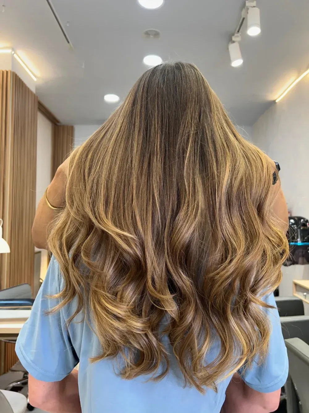 Persona con cabello largo, ondulado y con mechas, sentada en una silla de peluquería.