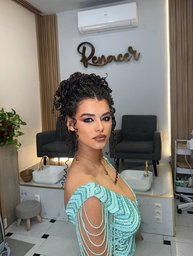 Mujer con vestido turquesa posando en un salón moderno con un letrero de neón y dos sillas negras al fondo.