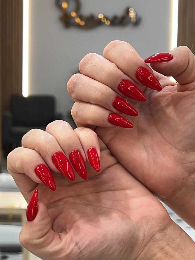 Manos con largas uñas rojas de aguja sostenidas contra un fondo interior borroso