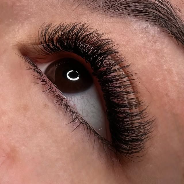 Primer plano de un ojo con largas pestañas oscuras y un brillante reflejo circular.