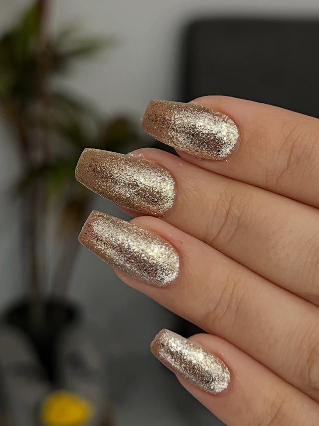 Primer plano de una mano con uñas largas de purpurina dorada metalizada.