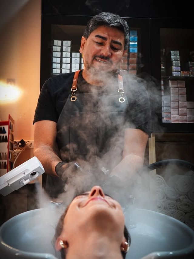 Lavado de cabello en una peluquería, con vapor que se eleva mientras un estilista enjuaga el cabello.