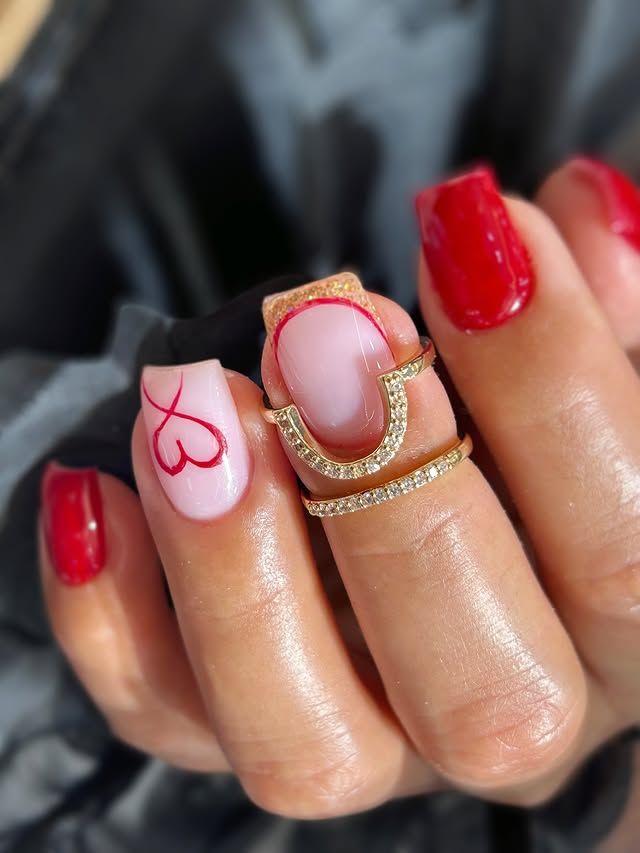 Mano con manicura roja y rosa pálido, dibujo lineal rojo en una uña y anillos dorados apilados.