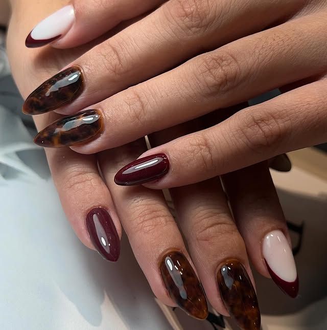 Manicura francesa con acentos florales burdeos sobre uñas en forma de almendra.