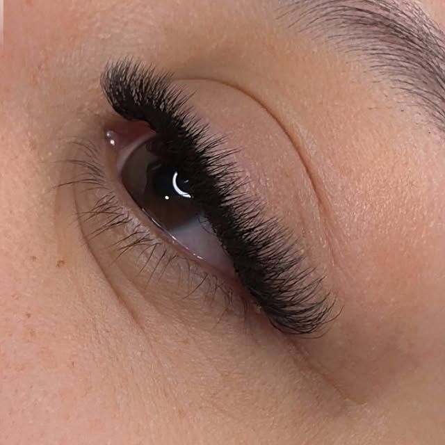 Primer plano de un ojo cerrado con largas extensiones de pestañas negras y maquillaje marrón suave.