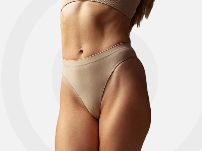 Torso de mujer en ropa interior beige, mostrando una cintura y caderas delgadas sobre un fondo claro.