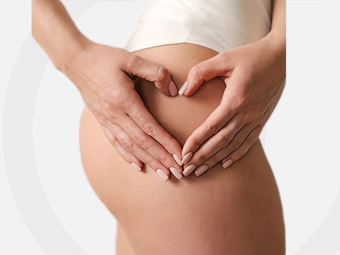 Manos formando un corazón sobre una barriga de embarazada.