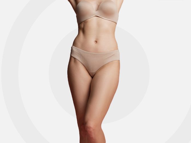 Mujer en lencería color nude de pie sobre un fondo gris claro.