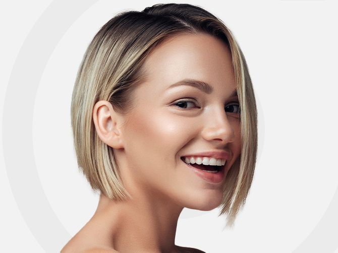 Persona sonriente con cabello rubio corto sobre un fondo claro.