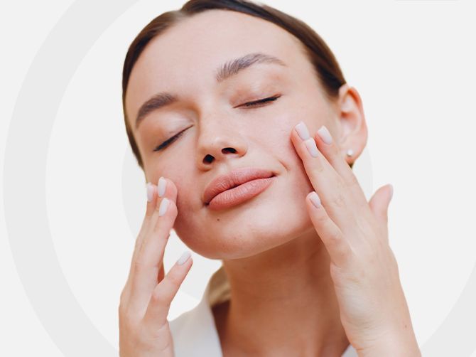 Mujer aplicándose crema en la cara con los ojos cerrados.