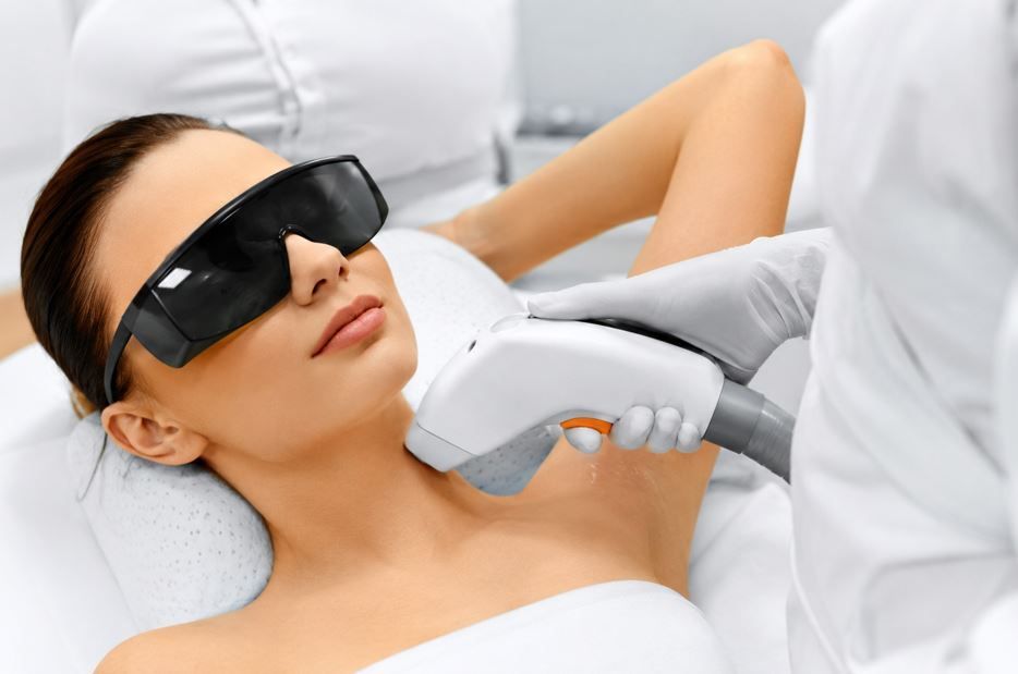 Mujer con gafas protectoras recibiendo un tratamiento láser cosmético en el cuello.
