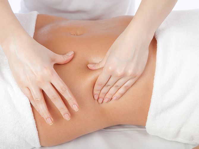 Unas manos masajean suavemente un abdomen sobre un fondo de toalla blanca.