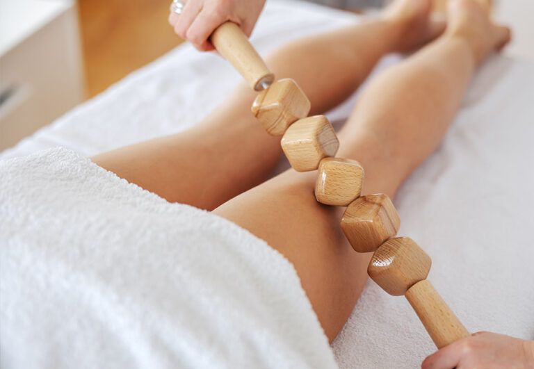 Herramientas de masaje de madera deslizándose sobre las piernas de una persona sobre una toalla blanca.