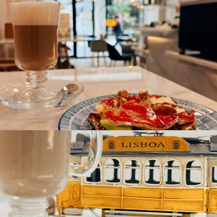 Café y bollería sobre una mesa de cafetería, con un tranvía amarillo de Lisboa reflejado en el cristal de abajo.