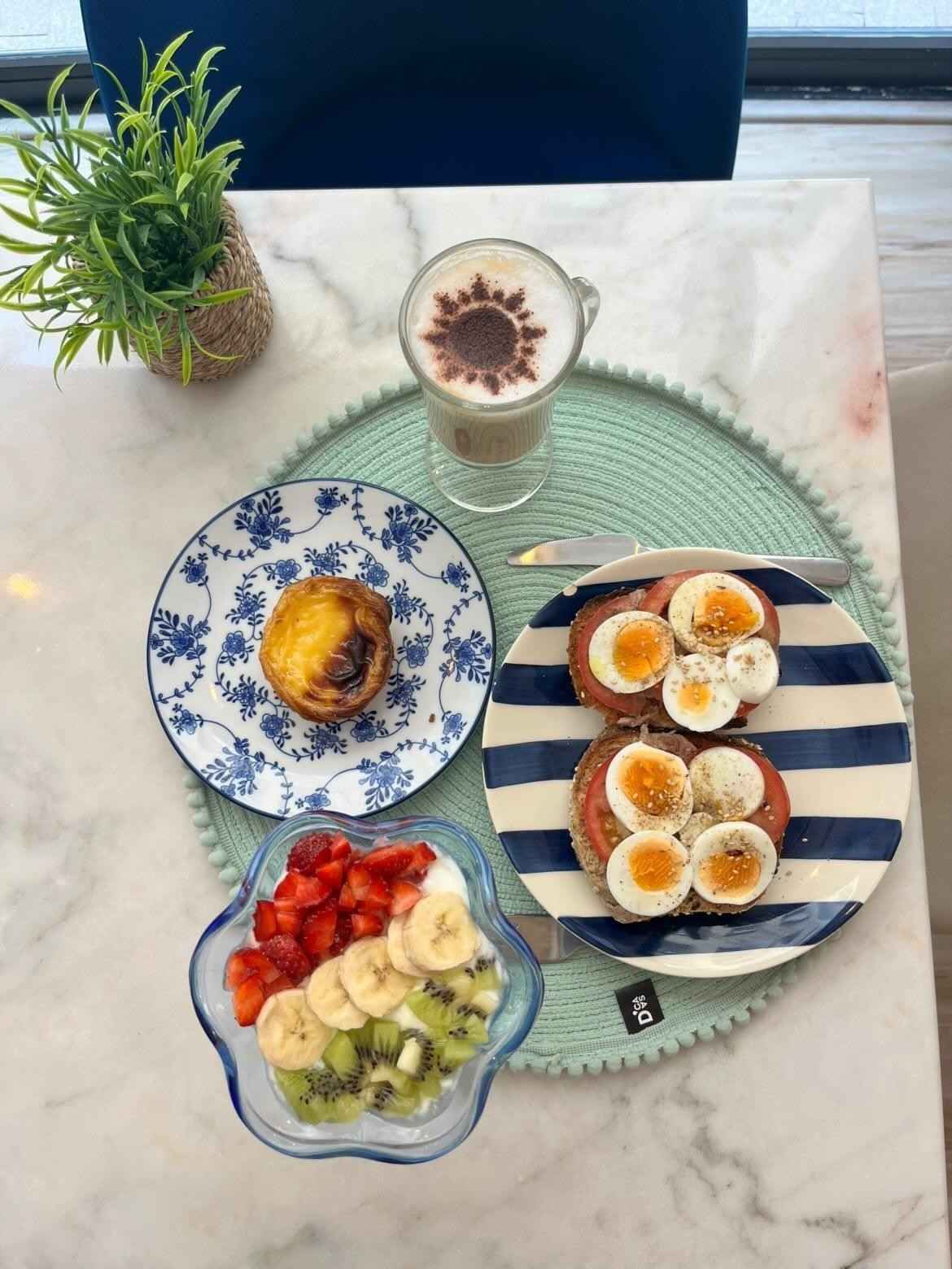 Brunch servido sobre una mesa de mármol con fruta, tostadas y una bebida de café en platos decorados.