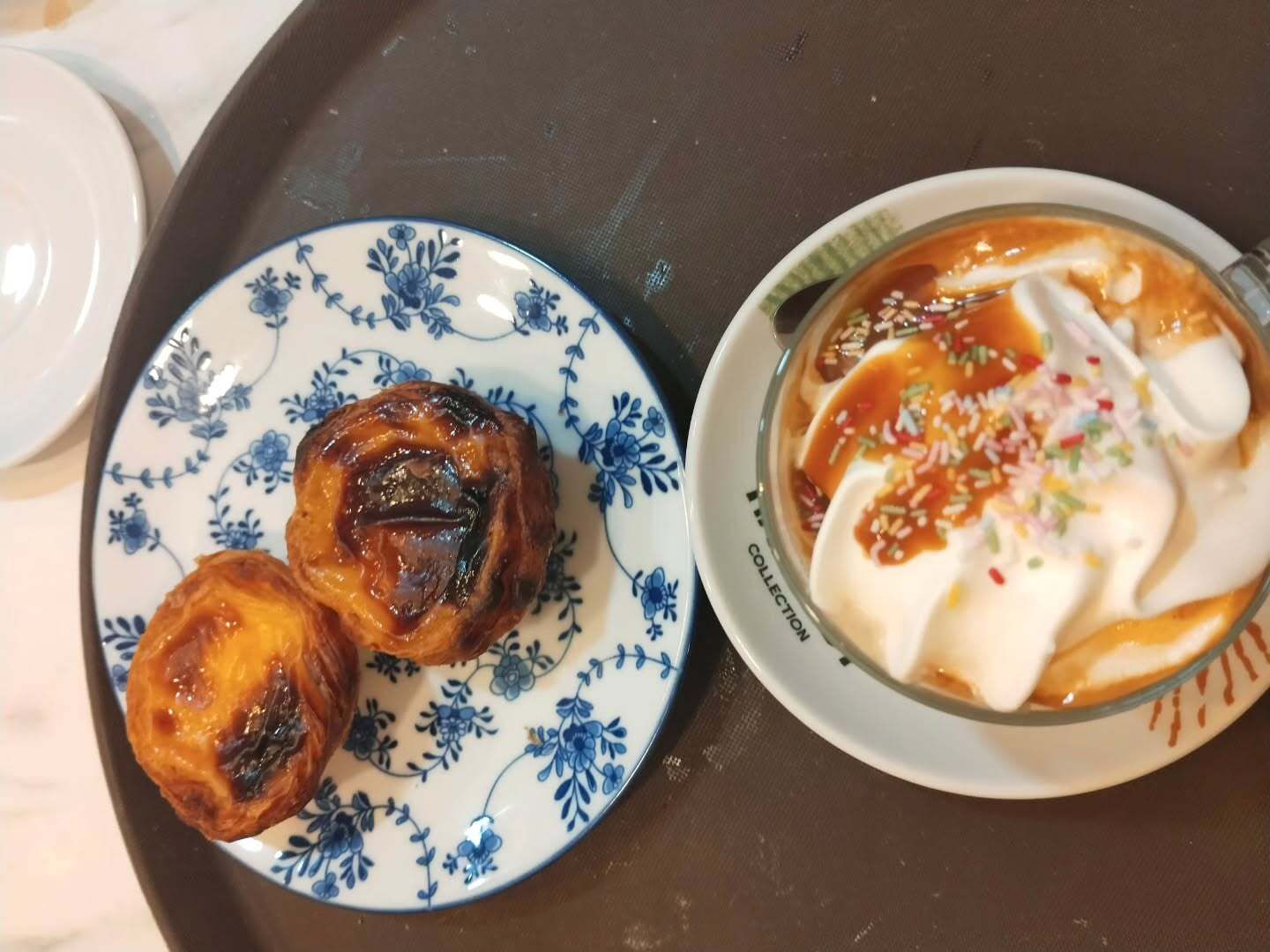Dos pasteles en un plato azul con estampado floral junto a un tazón de postre cremoso en una bandeja.
