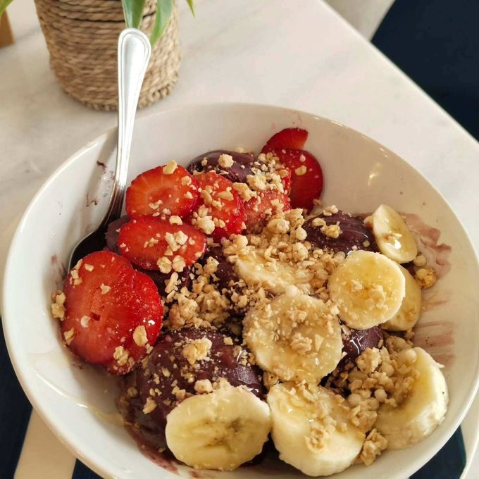 Un tazón de yogur cubierto con rodajas de plátano, fresas, granola y una cuchara sobre una mesa.